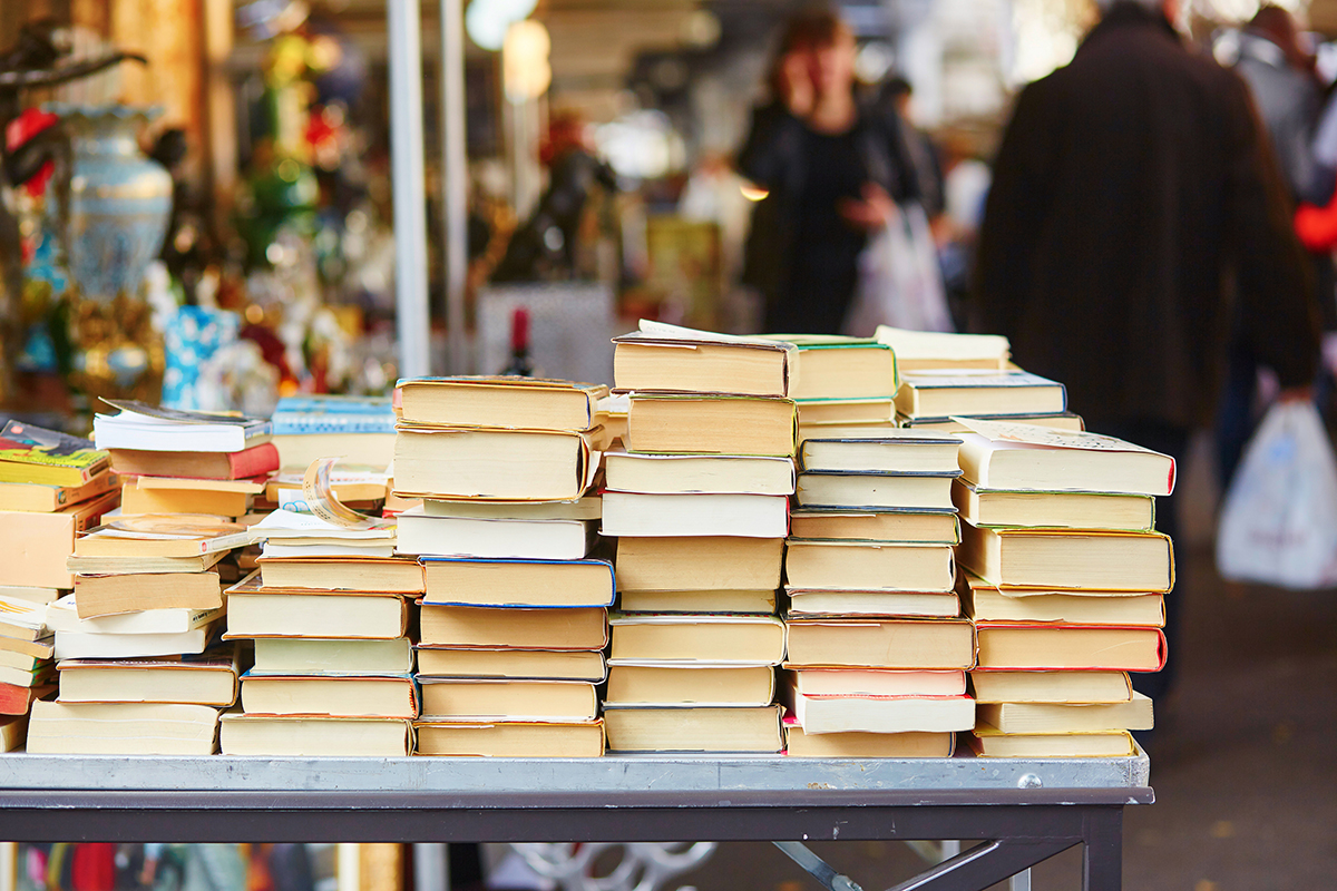 Old books piled on a table at an outdoor used book sale.